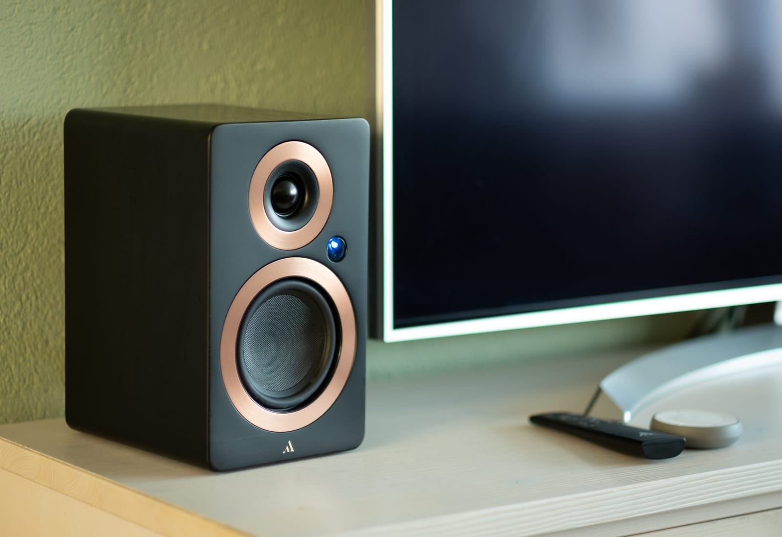 Caixa de som hi-fi vista de perto, com tweeter e woofer em destaque, e um televisor ao fundo