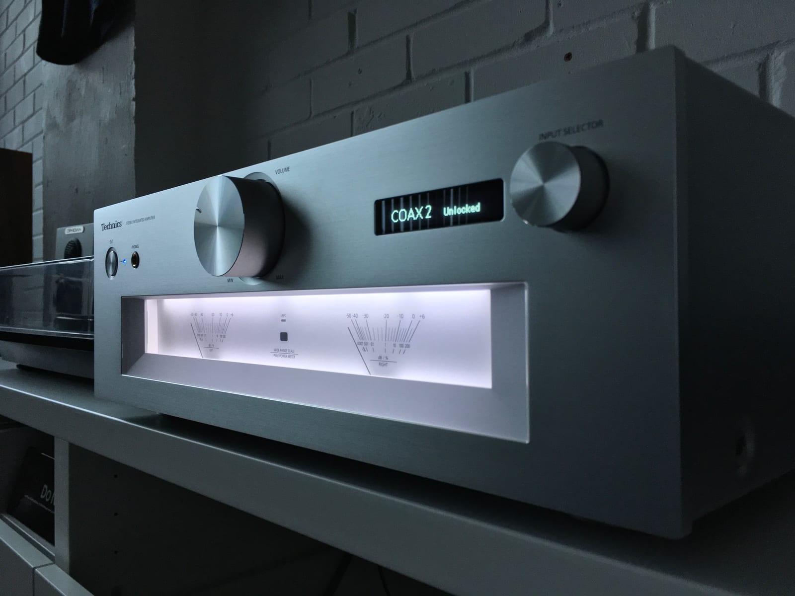 Amplificador integrado de som com painel prateado, botões de volume e visor iluminado